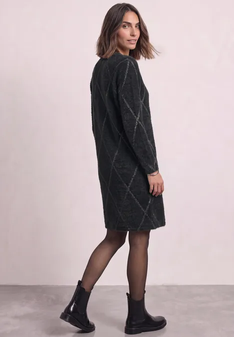 Robe à carreaux arrivant aux genoux armor grey Femme en robe-pull noire à motif losange, regarde par-dessus l’épaule, porte collants et bottines noires.