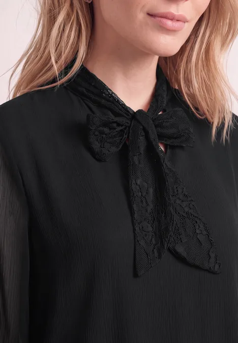 Nahe Aufnahme einer Frau in schwarzer Bluse mit filigraner Spitzen-Schleife am Kragen.