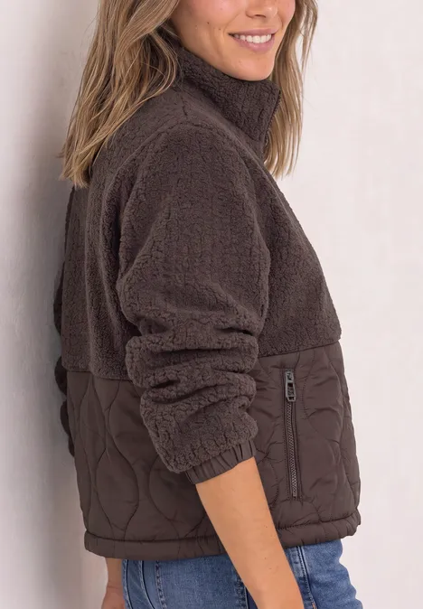 Frau im Profil in brauner Fleecejacke mit Steppbesatz, lächelt freundlich.