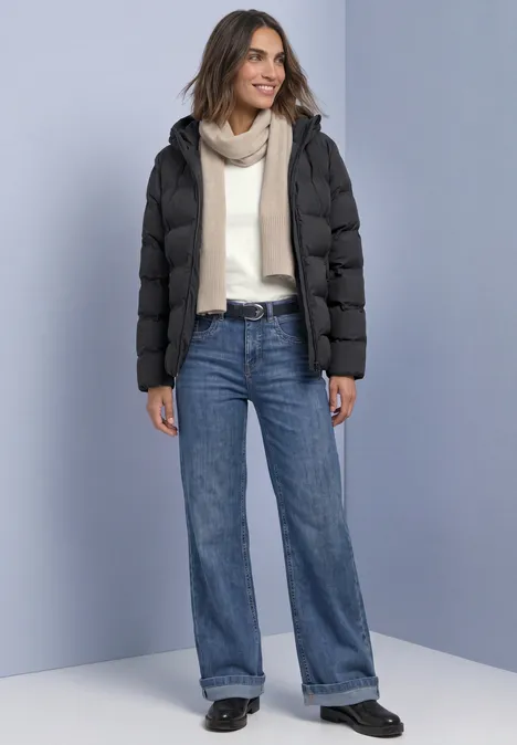 Frau trägt schwarze Daunenjacke, hellen Pullover, Schal und weite Jeans.