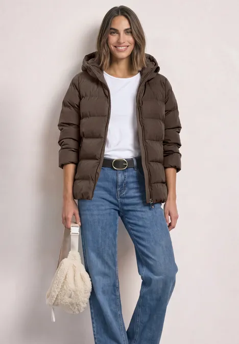 Frau im braunen Steppmantel, weißem T-Shirt, blauen Jeans und flauschiger Tasche.