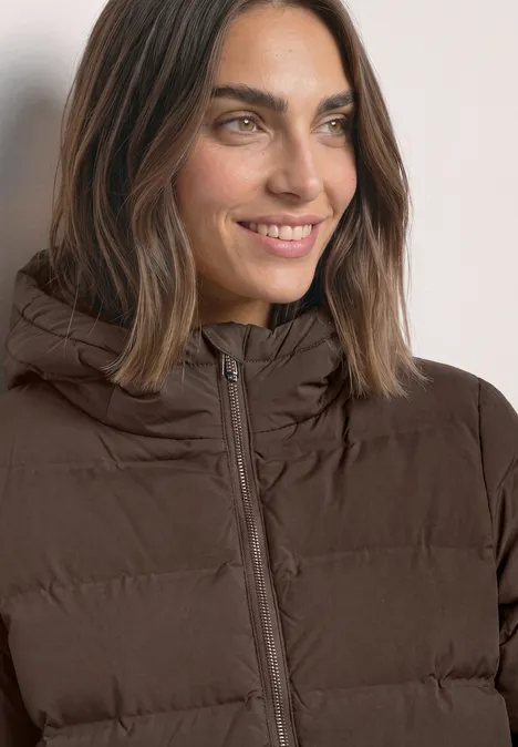 Nahaufnahme einer lächelnden Frau in brauner Steppjacke mit Kapuze.