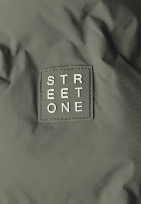 Ein olivgrüner Stoffpatch mit der weißen Aufschrift 'STREET ONE' auf einer Jacke.