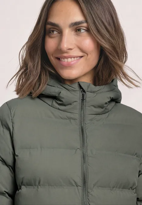 Frau in olivgrüner, gesteppter Winterjacke mit Kapuze, lächelnd.