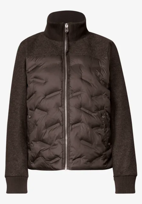 Veste hybride noire avec corps matelassé, manches en maille et fermeture éclair centrale.