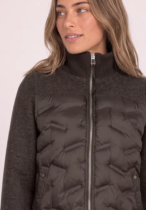 Femme porte une veste matelassée noire avec un corps en duvet, manches en maille et col montant.