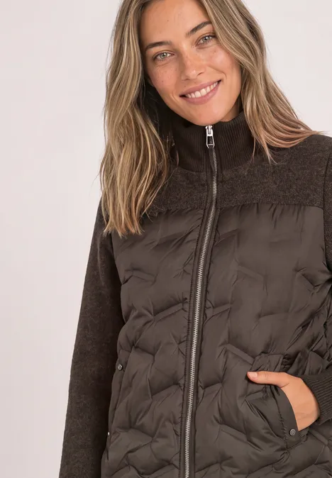 Frau in brauner, gesteppt-Jacke mit Reißverschluss und Fleeceärmeln, die lächelnd in die Kamera blickt.