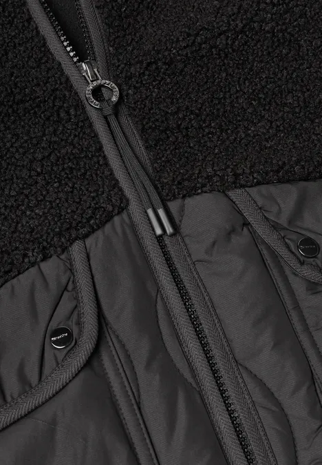 Nahaufnahme eines schwarzen Jackenoberteils mit Teddy-Fleece, Nylonpasse und durchgehendem Reißverschluss.