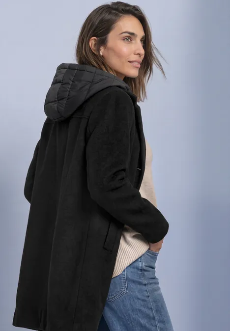 Manteau à col à revers et capuche intégrée Black Une femme de profil porte un manteau à capuche noir.