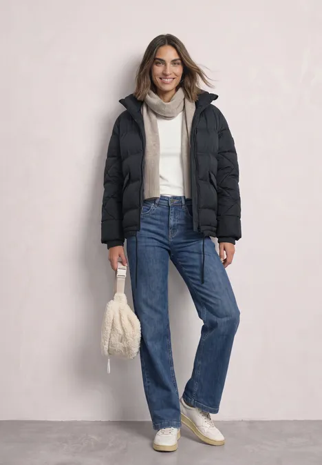 Steppjacke mit Stehkragen und Tunnelzug Obsidian Blue Dame trägt winterliche Daunenjacke, Jeans und Beanie, hält weiße flauschige Tasche.