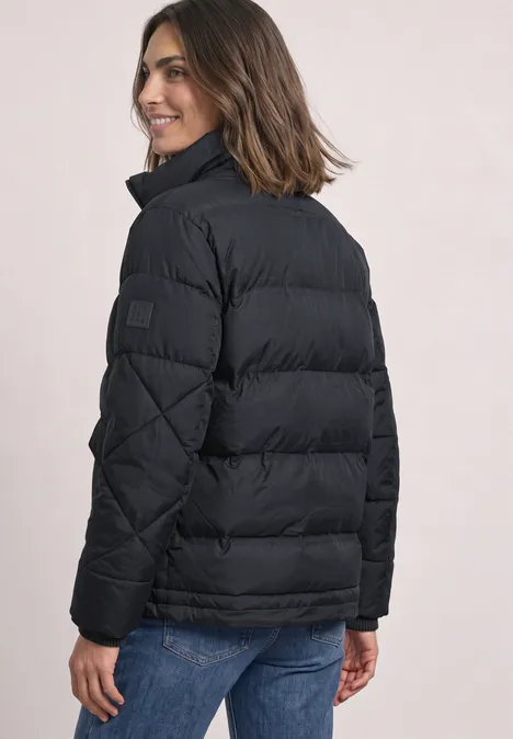 Steppjacke mit Stehkragen und Tunnelzug Obsidian Blue Frau von hinten in schwarzer Steppjacke und blauer Jeans, sie lächelt über die Schulter.