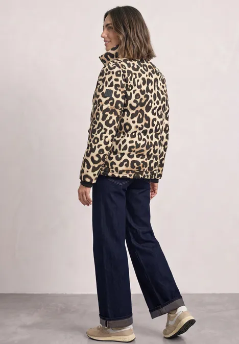 Vrouw met luipaardprintjas, wijde jeans en sneakers voor een lichte achtergrond.