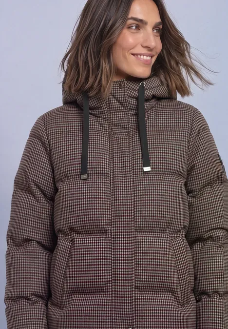 Frau in braun kariertem, wattiertem Winterparka mit Kapuze und aufgesetzten Taschen.