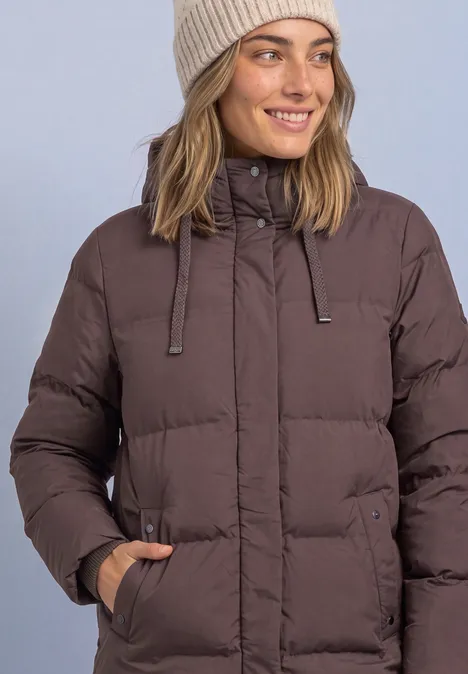 Frau in brauner, wattierter Winterjacke mit Kapuze und Beanie lächelt