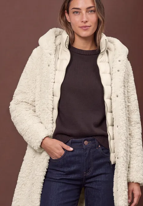 Frau in dunklem Pullover und Jeans mit cremefarbener, flauschiger Wattierung und Kapuze