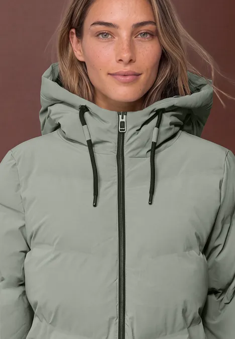 Eine Frau mit hellgrau-grüner Steppjacke mit Kapuze und Reißverschluss.