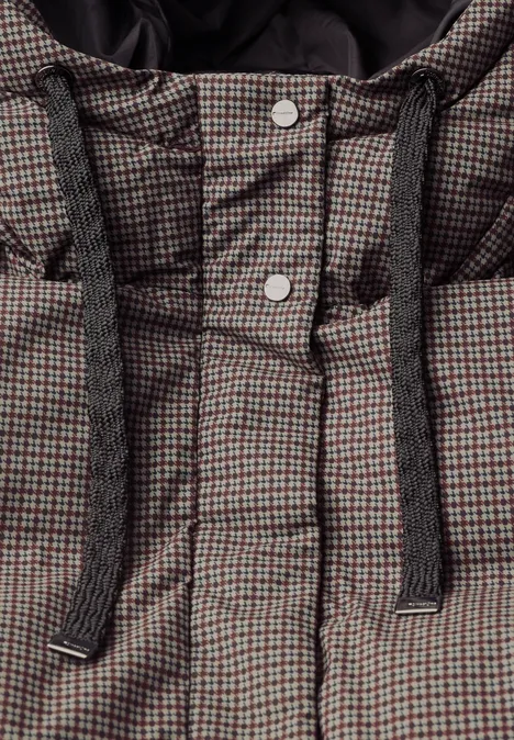Nahaufnahme einer karierten, wattierten Jacke mit Kapuze und dicken, schwarzen Kordeln sowie silbernen Druckknöpfen.