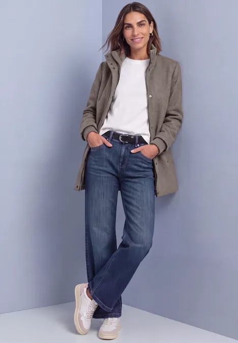 Kurzer Mantel mit Strickdetails Muddy Mocha Melange Frau in grauem Mantel, weißem Shirt, blauen Jeans und weißen Sneakern steht entspannt, lehnt an Wand.
