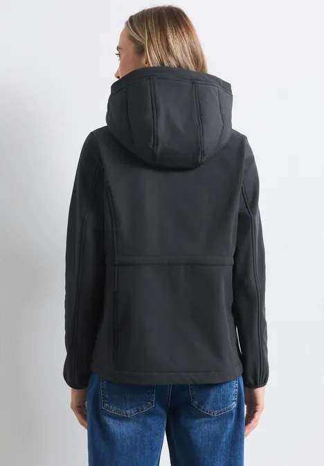 Rückansicht einer Person in schwarzer Kapuzenjacke und blonden Haaren, trägt blaue Jeans.