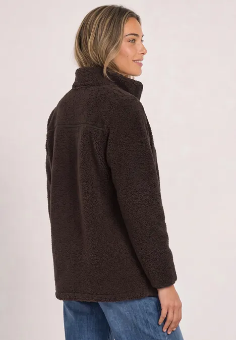 Frau in dunkelbrauner Teddy-Fleecejacke mit Stehkragen, seitlich im Profil, dazu blaue Jeans.