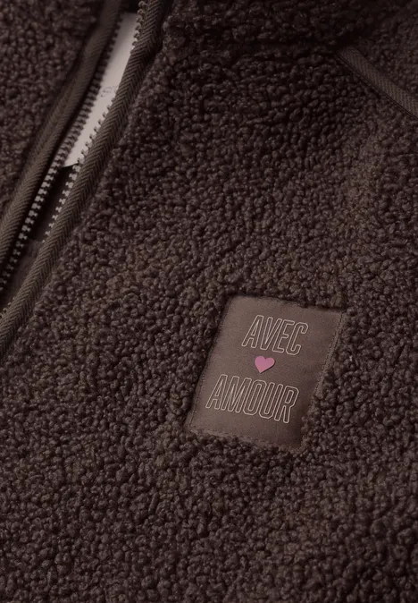 Ein brauner Teddy-Fleece mit Reißverschluss und einem Patch mit Schriftzug 'Nice Amour' und rosa Herz.
