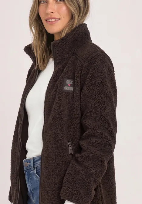 Frau in brauner Teddy-Fleecejacke mit Reißverschluss, kombiniert mit weißem Top und Jeans.