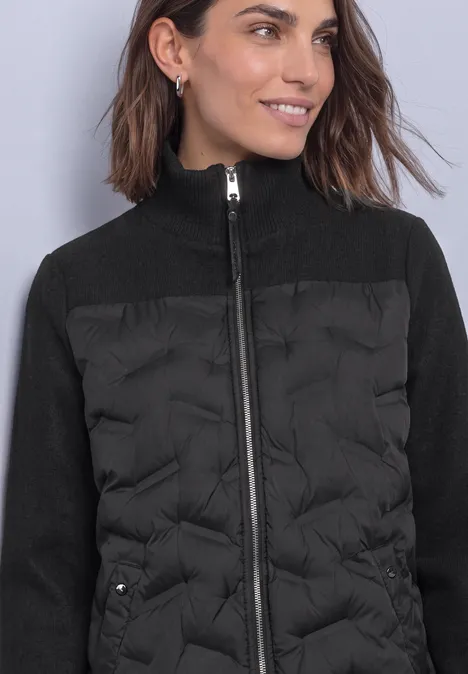 Strukturmix Jacke mit geklebter Steppung Black Frau trägt schwarze, gesteppt-vorn und gestrickte Ärmel-Jacke mit hohem Kragen, lächelnd seitlich blickend.