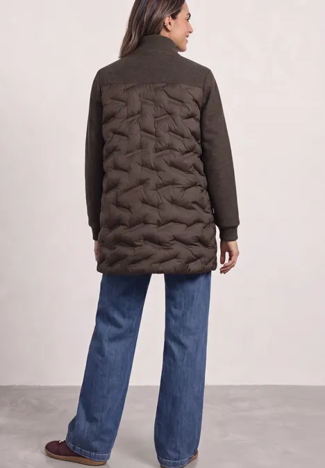 Strukturmix Jacke mit geklebter Steppung auburn brown Eine Frau von hinten in dunklem Steppmantel mit Zopfmuster auf dem Rücken, weite Jeans und Schuhe.
