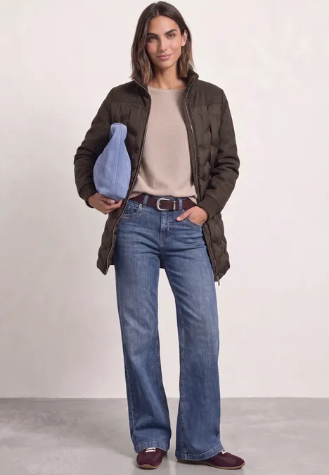 Strukturmix Jacke mit geklebter Steppung auburn brown Frau in olivgrünem Steppmantel, beigem Pullover, ausgestellten Jeans, bordeauxfarbigen Loafers und hellblauer Tasche.