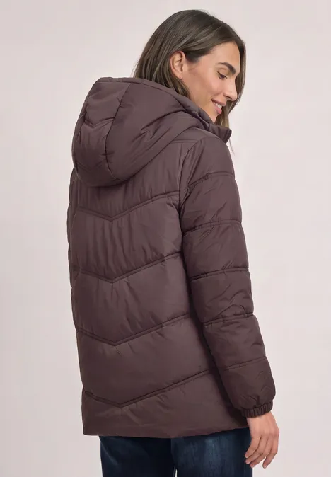 Frau mit brauner Steppjacke und Kapuze blickt seitlich, Rückenansicht.
