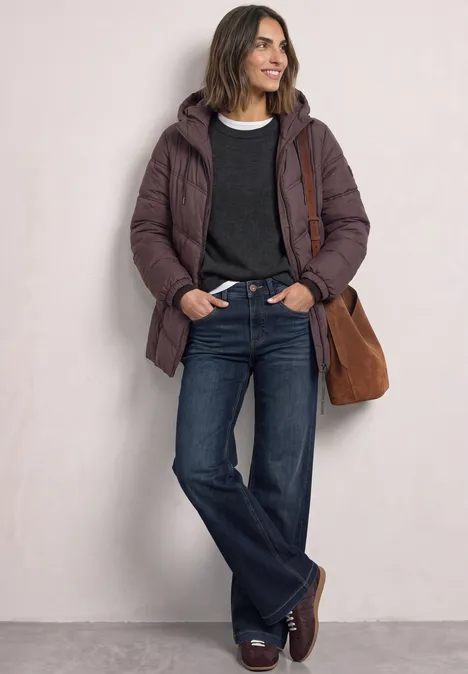 Frau in brauner Steppjacke, dunkelblauem Pullover, Jeans und braunen Schuhen mit passender Tasche