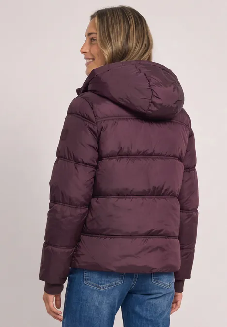 Rückenansicht einer Person in einer lilafarbenen Steppjacke mit Kapuze und Jeans.