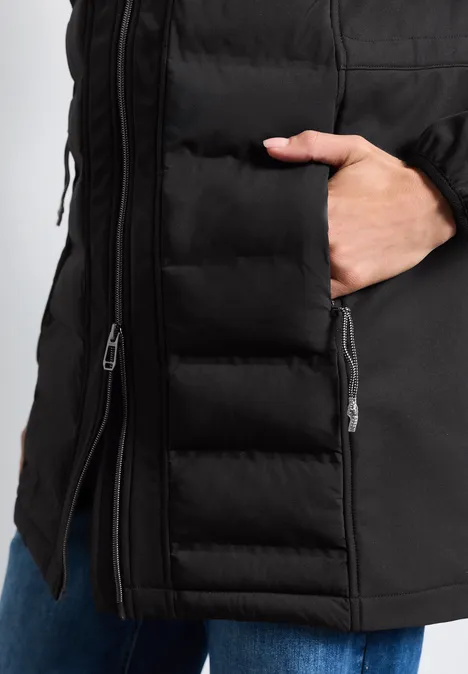 Veste matelassée noire avec fermeture éclair, main dans la poche latérale.