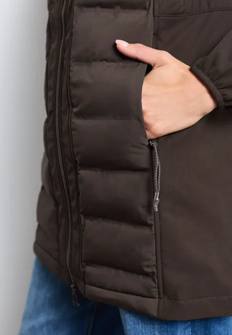 Detailaufnahme einer dunkelbraunen Steppjacke mit seitlichem Reißverschluss und Hand in der Tasche.