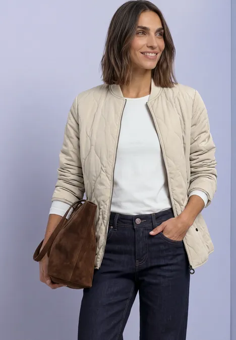 Blouson met doorgestikt patroon en ritssluiting barley beige Vrouw in beige doorgestikte jas, wit shirt en blauwe jeans, met een bruine suède tas.