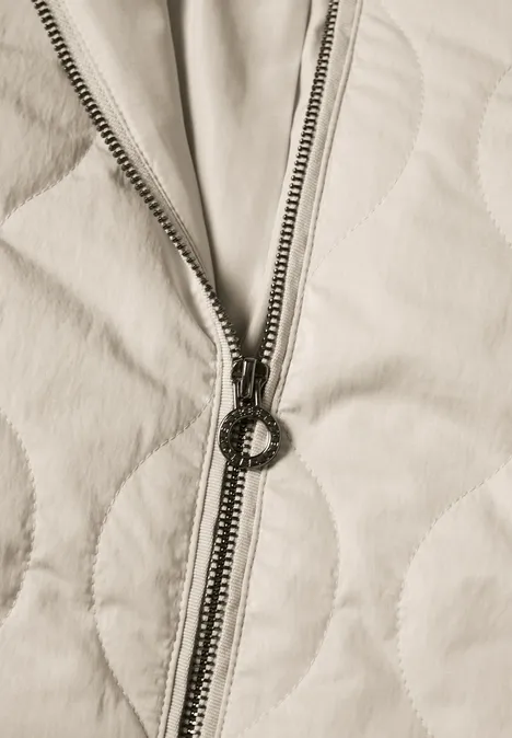 Blouson met doorgestikt patroon en ritssluiting barley beige Close-up van een licht doorgestikt stof met een ronde metalen rits.