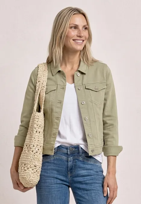 Frau trägt grüne Jacke, weißes Shirt, blaue Jeans und eine gehäkelte Schultertasche.