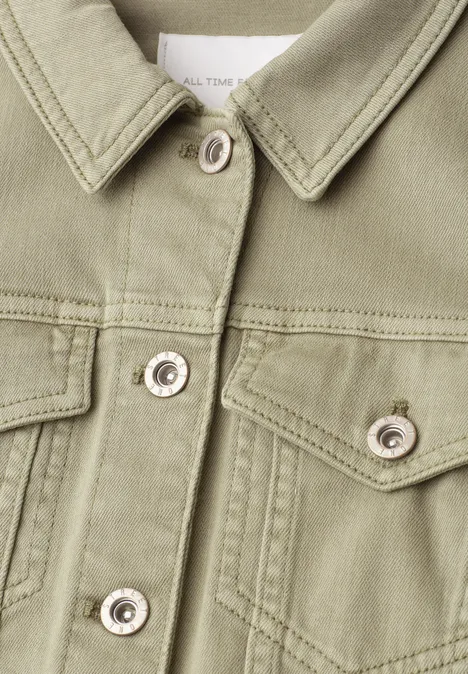 Nahaufnahme einer olivgrünen Jeansjacke mit Hemdkragen, Brusttaschen und silbernen Druckknöpfen.