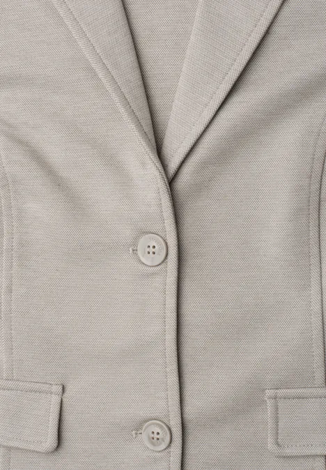 Close-up van een beige blazer met knopen en zakken.