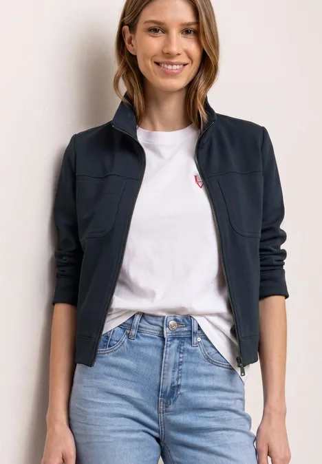 Eine Person trägt ein weißes T-Shirt, blaue Jeans und eine dunkelblaue Jacke.