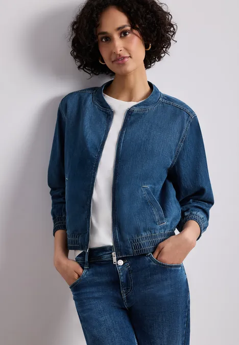 Denim-look blouson met ritssluiting Medium Blue washed Persoon met krullend haar draagt een spijkerjasje, wit T-shirt en jeans, handen in de zakken.