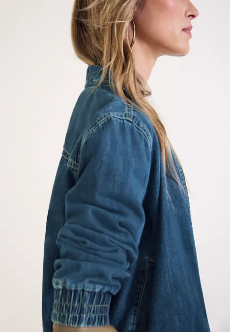 Denim-look blouson met ritssluiting Medium Blue washed Zijaanzicht van een vrouw met lang blond haar en een spijkerjas tegen een lichte achtergrond.