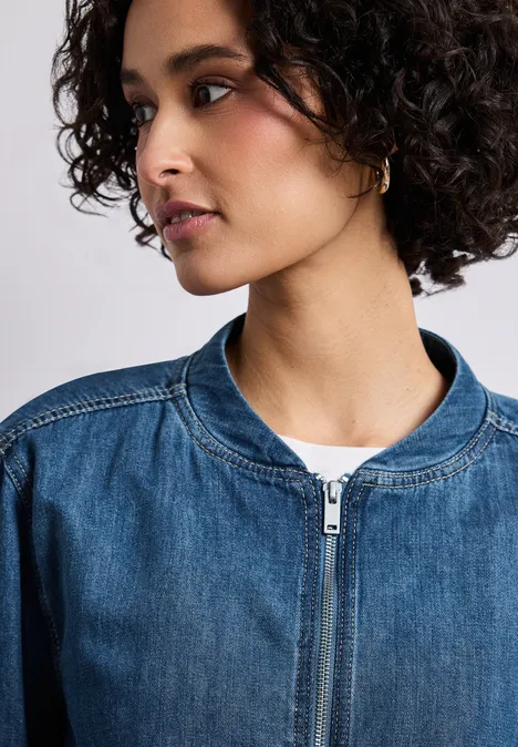 Denim-look blouson met ritssluiting Medium Blue washed Close-up van een vrouw met krullend haar in een denim jasje en wit shirt, zijaanzicht.