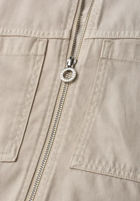 Close-up van een beige jack met rits en opgestikte zakken.