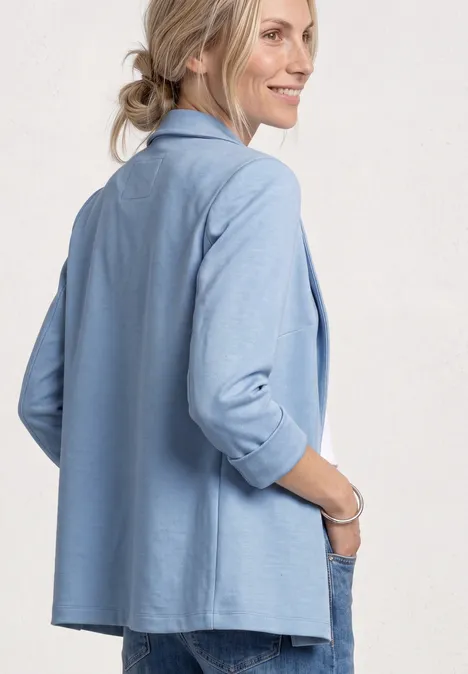 Vue arrière d’une femme portant un blazer bleu clair aux manches retroussées.