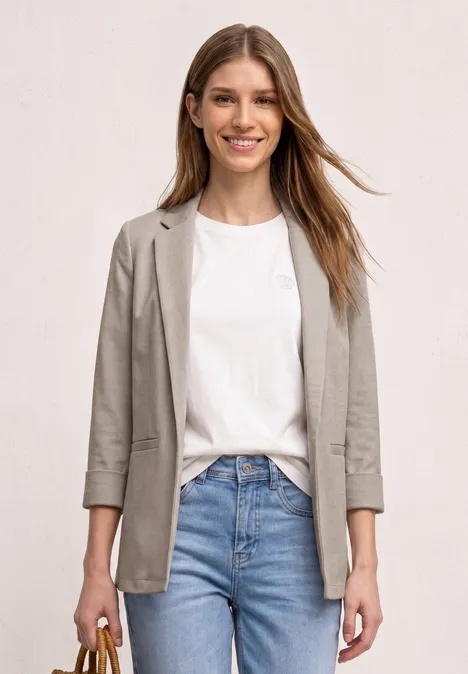Femme portant un t-shirt blanc, un blazer gris et un jean bleu sur fond clair