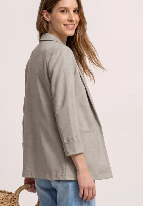Femme en veste grise décontractée, vue de profil sur fond clair.