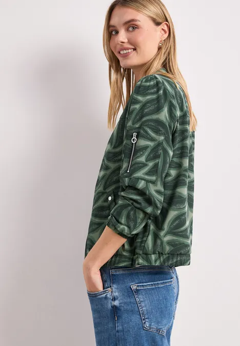 Seitliche Aufnahme einer Person in grün gemustertem Pullover und Jeans, Gesicht unscharf.