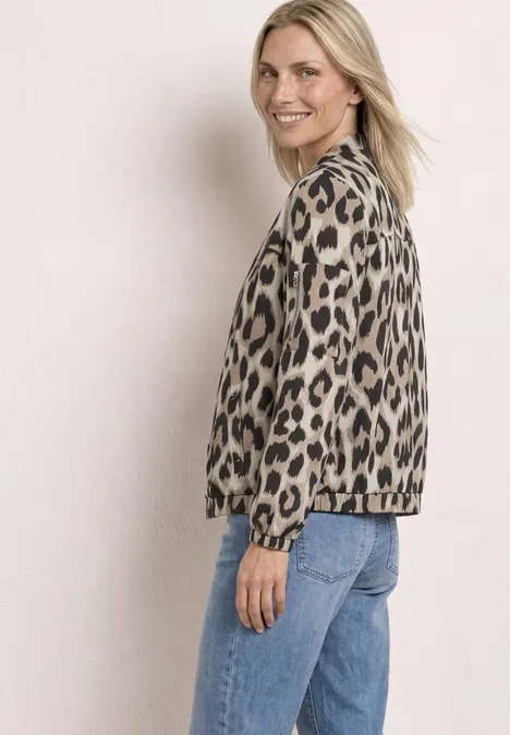 Femme de profil portant une veste léopard et un jean bleu sur fond clair.