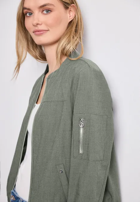 Vrouw in groene bomberjas met ritssluitingzak op de mouw en een wit hemd